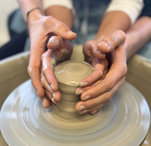 Image shows two pairs of hands, shaping clay on a potter's wheel at World of Wedgwood, Stoke-on-Trent